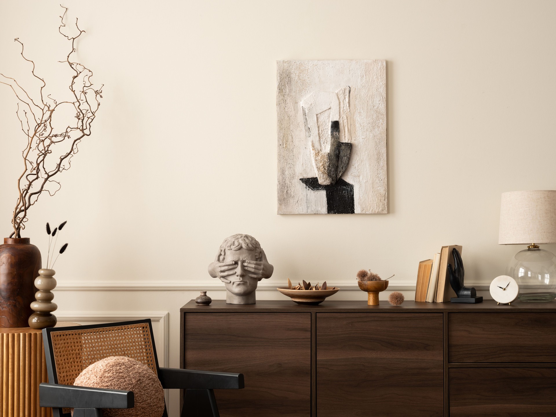 Creative composition of stylish living room interior with mock up poster frame, wooden sideboard, vase with branch, rattan chair, lamp, sculpture and personal accessories. Home decor. Template.